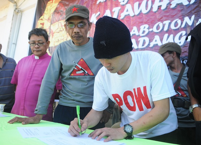 20soldier2 FREED. After 133 days in captivity, Army PFC. Adonis Jess Lupiba (in white shirt) signs his release papers from his NPA captors in barangay Kaulayanan, Sugbongcogon town in Misamis Oriental on Nov. 20, 2015. Lupiba was captured by the rebels after a brief firefight in Barangay Alagatan, Gingoog City last July 11, 2015. MindaNews photo by Froilan Gallardo 