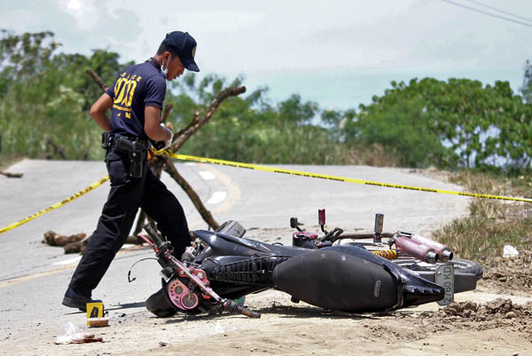 CRIME SCENE. A police investigator checks a damaged motorcycle for evidence in Barangay Bit-os, Butuan City on August 6, 2012. The vehicle was used by one police officer who died and another who was wounded when suspected communist rebels ambushed them on the same day. MindaNews photo by Erwin Mascarinas