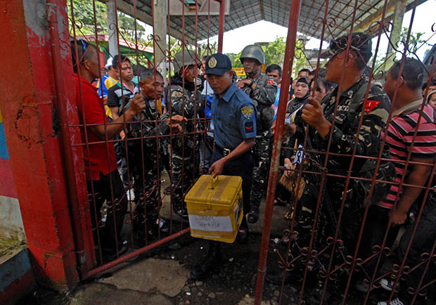 A police officer carries a ballot box as Army soldiers watch the gates at the Panderanao Primary School in Tugaya town in Lanao del Sur on Election Day, Oct. 28, 2013. MindaNews photo by Froilan Gallardo