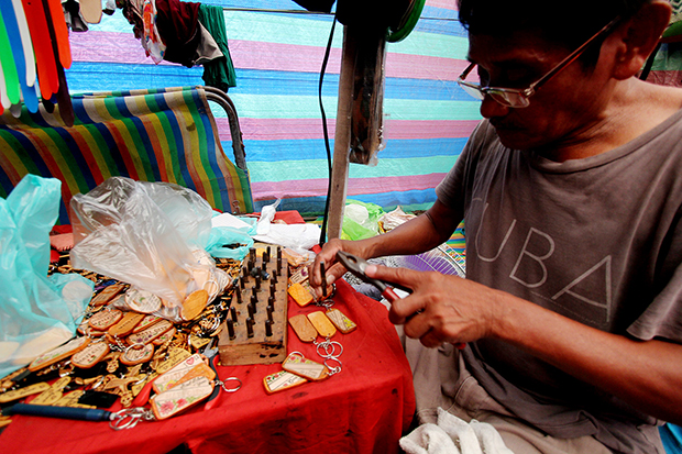 Pio Baturiano from Manila punches letters on a keychain souvenir in his shop on Wednesday (May 6) at the Davao del Norte Sports and Tourism Complex in Tagum City during the Palarong Pambansa 2015. Mindanews Photo by Keith Bacongco
