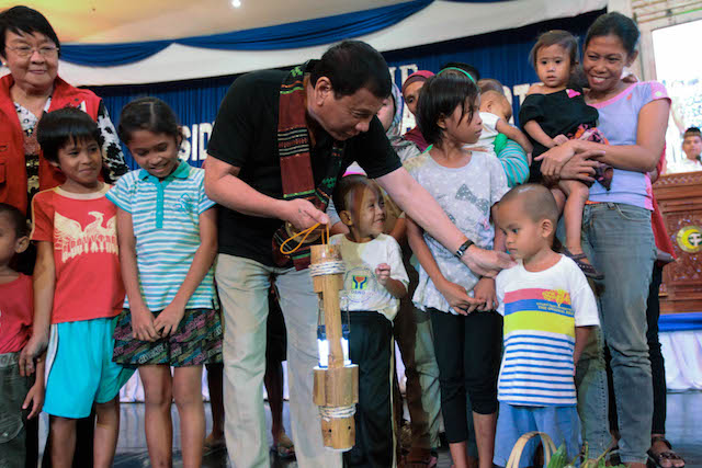 Social Welfare Secretary Judy Taguiwalo watches as President Rodrigo Duterte, holding the symbolic lamp representing the commitment of various agencies to address hunger, particularly among children in the Autonomous Region in Muslim Mindanao (ARMM), interacts with the children during the launch of the Comprehensive Reform and Development Agenda for ARMM and conflct-affected areas in Regions 9, 10 and 12 at the Shariff Kabunsuan Cultural Complex in Cotabato City on October 29. ACE MORANDANTE/Presidential Photo 